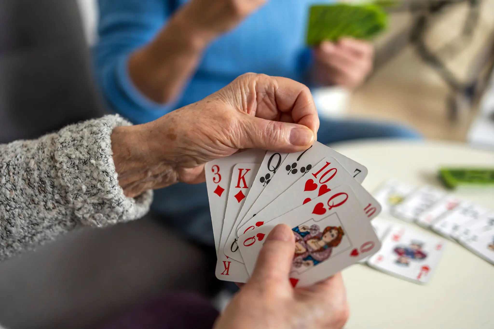 Older woman playing cards at a table, with a blurred background